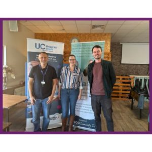 Three people stand in front of Universal Credit and Community Money Advice banners at a community event (Benefits Café on Migration from ESA to UC).